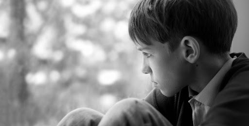 Sad teenager sitting on window, black-and-white photo