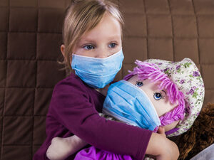 Girl in a medical mask playing doctor with her toys.