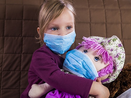 Girl in a medical mask playing doctor with her toys.